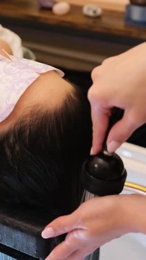 Kuaför, profesyonel bir kuaförde uzun siyah saçlı bir kadını duş başlığıyla duruluyor.