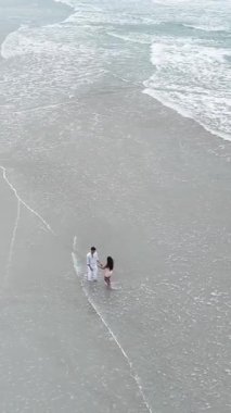 Güzel, boş bir plajda birbirini kucaklayan romantik bir çiftin yüksek açılı görüntüsü.