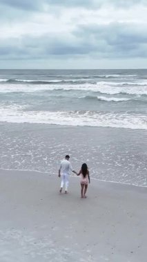 Bulutlu bir günde sahilde çıplak ayakla yürürken el ele tutuşan genç çift.