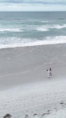 Bulutlu bir günde kıyı boyunca el ele yürüyen genç bir çiftin yüksek açılı görüntüsü