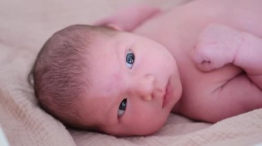 Yumuşak bir battaniyeye uzanmış, etrafa bakan büyük mavi gözleri olan güzel bir bebeğin yakın çekimi.