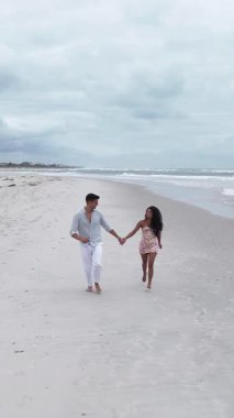 Mutlu genç melez çift tatillerinde kumlu sahilde koşuyor ve gülümsüyor.