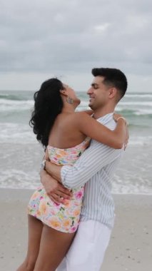 Genç ve sevgi dolu bir çift, sahilde kucaklaşırken samimi ve mutlu bir anı paylaşıyor.