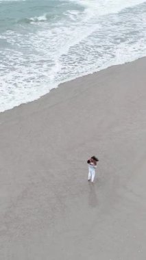 Genç ve sevgi dolu bir çiftin güzel bir deniz kıyısında dalgalarla dans edişinin havadan görüntüsü.