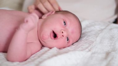 Küçük yeni doğmuş bebek kız yumuşak beyaz bir battaniyenin üzerinde uzanırken esniyor ve komik suratlar yapıyor.