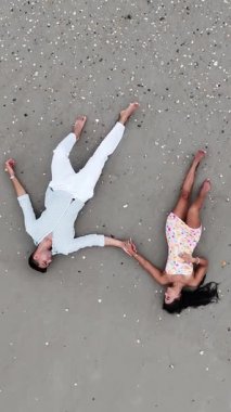 Kumlu bir kumsalda el ele tutuşan genç bir çiftin yukarıdan aşağı görüntüsü.