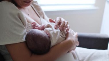 Yeni anne yeni doğmuş bebeğini kucağına alıp emziriyor, hassas ve samimi bir bağ kuruyor.