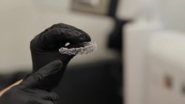 Siyah tıbbi eldivenli ortodontist ısırık düzeltmesi için şeffaf bir diş teli tutuyor.