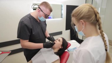 Modern bir klinikte genç bir kadının dişlerini kontrol eden bir dişçi ve hemşire ile diş muayenesi.