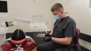 Modern bir klinikte diş tedavisi için şırınga hazırlayan profesyonel bir erkek dişçi.