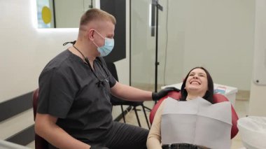 Modern bir klinikteki randevusu sırasında dişçisiyle konuşan genç bir kadın.