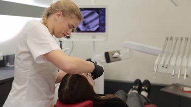 Klinikte genç bir kadının dişlerini modern aletlerle muayene eden profesyonel bir dişçi.
