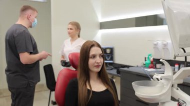 Modern stomatoloji kliniğinde diş muayenesi sırasında kameraya konuşan genç bir kadın.