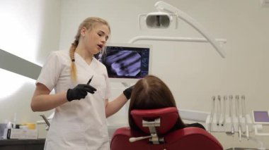 Dişçi bir hastaya tedavi planını anlatıyor. Klinikteki bir monitörde röntgen kullanıyor.