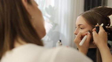 Vizör makyaj yapıyor ve güzellik salonunda genç ve güzel bir kadın için saç stili yapıyor.