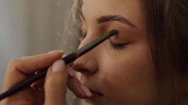 Profesyonel makyaj sanatçıları bir güzellik salonunda genç bir kadının gözüne göz farı sürüyor.