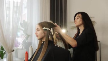 Profesyonel kadın kuaför, müşterilerine kuaförde uzun saç taraması yapıyor.