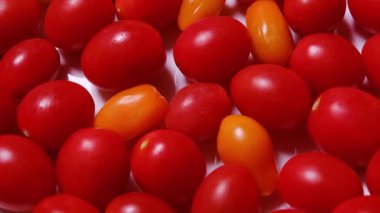 Taze kırmızı ve sarı kiraz domateslerinin yukarıdan görünüşü yavaşça beyaz arka planda dönüyor.