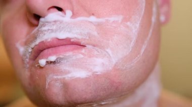 Günlük bakım rutini. Sakalını ve bıyığını köpük ve jiletle tıraş eden bir adam.