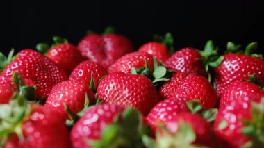 Sulu taze olgun çilekler siyah arka planda bir sepette dönüyorlar.