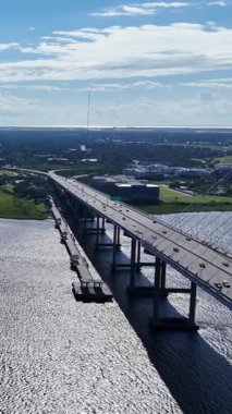 Güneşli bir günde, arka planda bir şehir olan parıldayan suyun üzerinde modern bir köprüde giden arabalar.