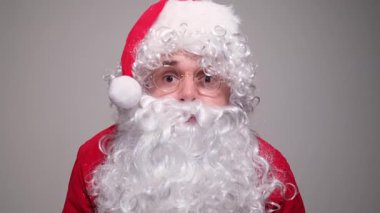 Kırmızı kostümlü, beyaz sakallı ve kameraya el sallayan Noel Baba karakterinin yakın çekimi.