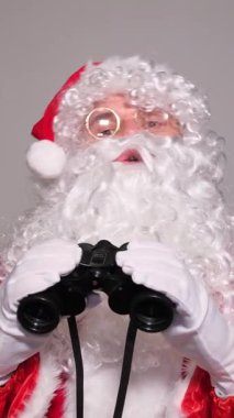 Geleneksel kırmızı takım elbiseli Noel Baba şok olmuş bir ifadeyle dürbünle bakıyor.