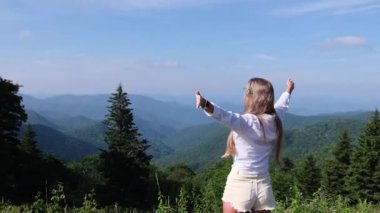 Kolları açık mutlu bir kadın güneşli bir günde güzel dağ manzarasının tadını çıkarıyor.