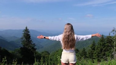 Arkasından genç bir kadın kollarını açıp dağların muhteşem manzarasının tadını çıkarıyor.