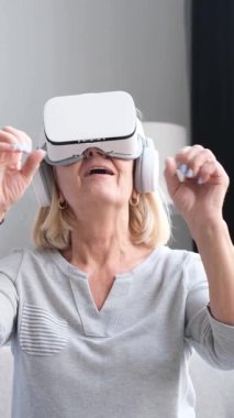 VR kulaklık takan, havaya dokunan ve gelişmiş gerçeklikte metaevreni keşfeden yaşlı bir kadın.
