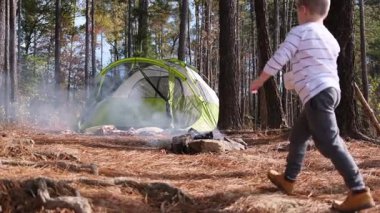 Genç çocuk ormandaki bir çadırın yakınındaki sigara içilen bir kamp ateşini söndürmek için bardaktan su döktü.