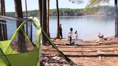 Çocuklu mutlu bir aile doğada birlikte vakit geçirir, gölün kenarında çadır kurar.
