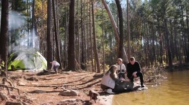 İki çocuklu mutlu bir aile ve güzel bir çam ormanında gölün kenarında kamp yapan bir köpek.