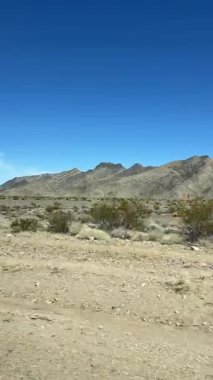 Güneşli bir günde hareket halindeki bir araçtan dağlarla kuru ve kurak bir çöl manzarası.