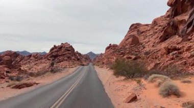 Kırmızı kaya oluşumlarıyla çevrili bir çöl otoyolu boyunca araba süren birinci şahıs manzarası