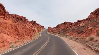 Manzaralı bakış açısı çöldeki kırmızı kaya oluşumlarının arasından geçen dolambaçlı bir yolda ilerliyor.