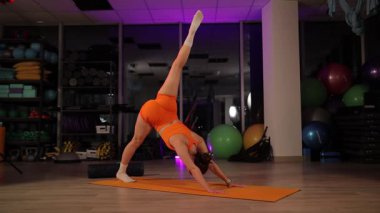 Genç atletik kadın zorlu bir yoga sekansı sergiliyor, aşağı doğru inen köpekten kol dengesine doğru akıyor.