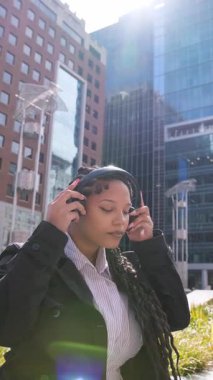 Afrika kökenli Amerikalı iş kadını kulaklık takıyor ve şehir merkezinde müziğin keyfini çıkarıyor.