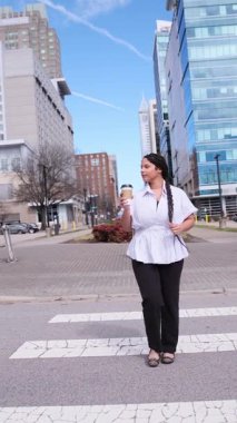 Modern bir şehirde yaya geçidinde yürüyen ve kahve içen genç, profesyonel Afro-Amerikan kadın.