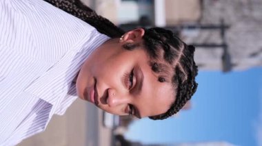 Saçları örgülü güzel Afro-Amerikalı kadın şehir ortamında güvenle gülümsüyor.