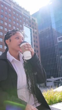 Genç Afrikalı Amerikalı iş kadını şehir merkezindeki modern bir şehirde kahve molası veriyor.