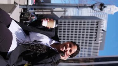 Arkasında gökdelenler olan bir kahve fincanı tutan mutlu Afrikalı Amerikalı kadın.