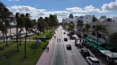 Miami sahilindeki sanat deco binaları, palmiye ağaçları ve trafik ile okyanus manzarası.