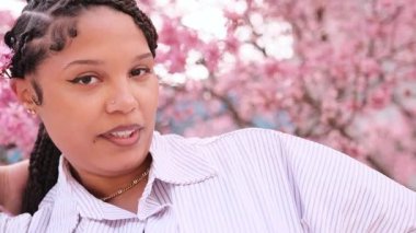 Saçları örgülü genç bir kadın, çiçek açan sakura ağaçlarıyla dolu bir parkta bahar gününün tadını çıkarıyor.