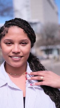 Saçları örgülü, genç ve mutlu bir kadın. Kenar mahallede dikilirken kendine güvenerek gülümsüyor.