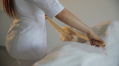 Kadın masör, güzellik salonunda özel bambu süpürgeleriyle bacak masajı yapıyor.