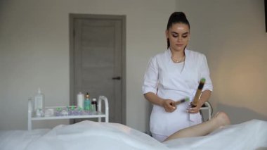 Modern bir kaplıca salonunda müşterinin bacağına bambu çubuklarıyla dokunan profesyonel bir güzellik uzmanı.