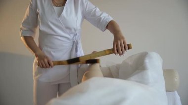 Profesyonel masöz, spa salonunda rahatlatıcı ve iyileştirici bir bacak masajı için bambu çubukları kullanır.