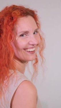 Kırmızı kıvırcık saçlı neşeli kadın omzunun üstünden bakıyor, gülüyor ve dilini dışarı çıkarıyor.