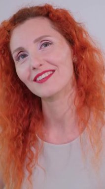 Kameraya gülümseyen kıvırcık kızıl saçlı çekici bir kadının yakın plan portresi.